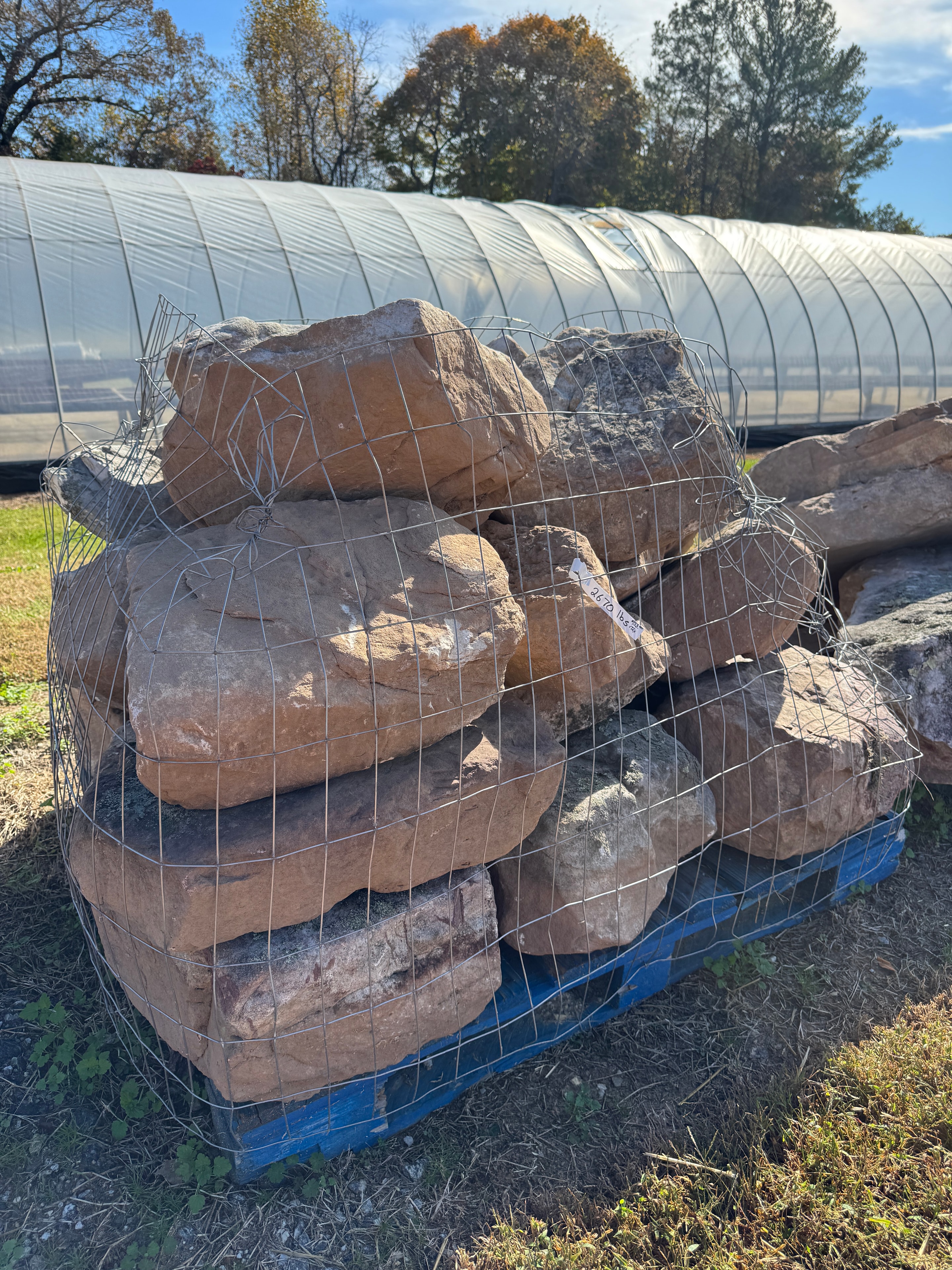 Wire-basketed pallet of large landscape boulders beside the greenhouse