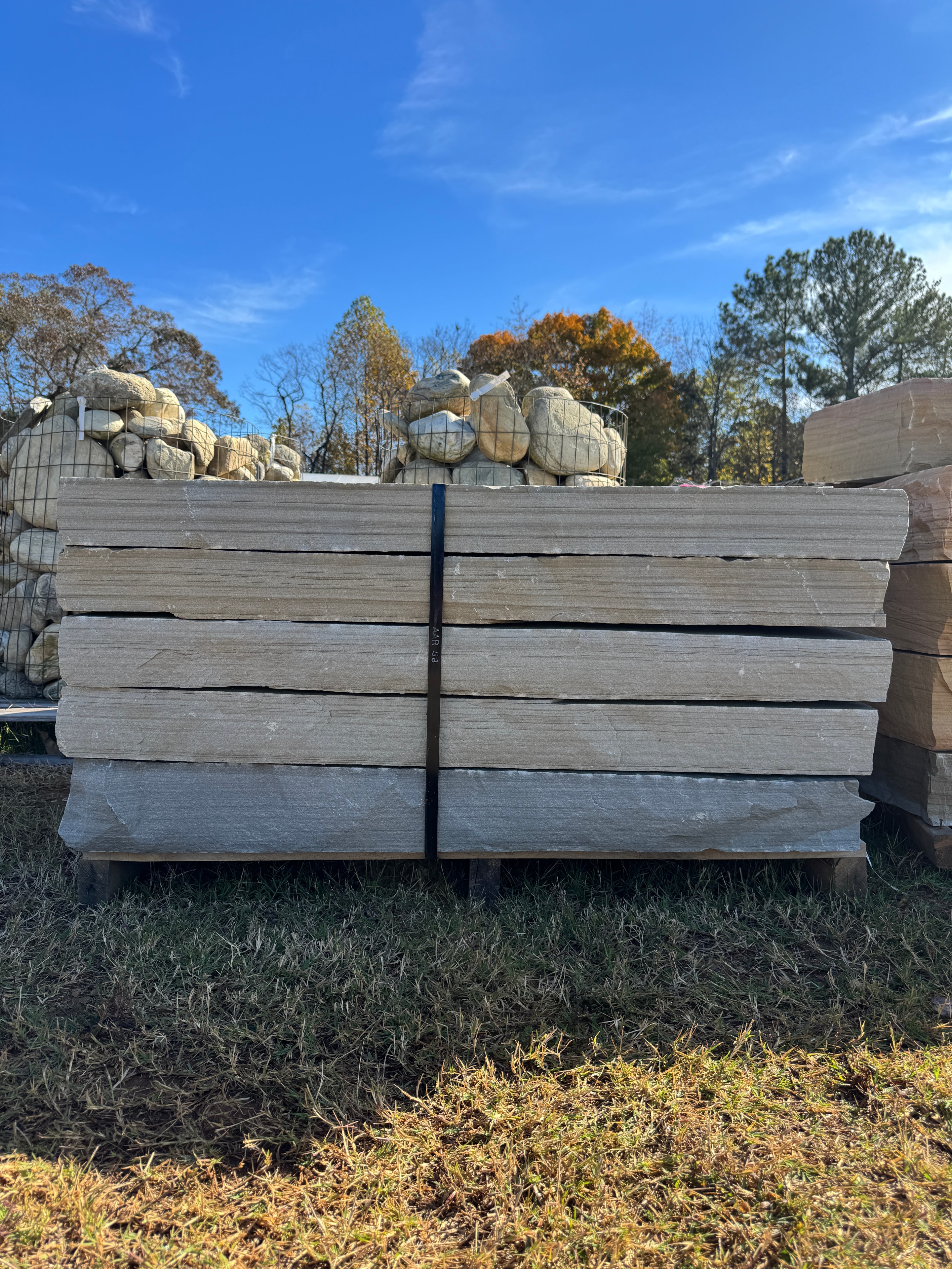 Pallet of stacked chocolate brown stone steppers with wire baskets of river rock behind