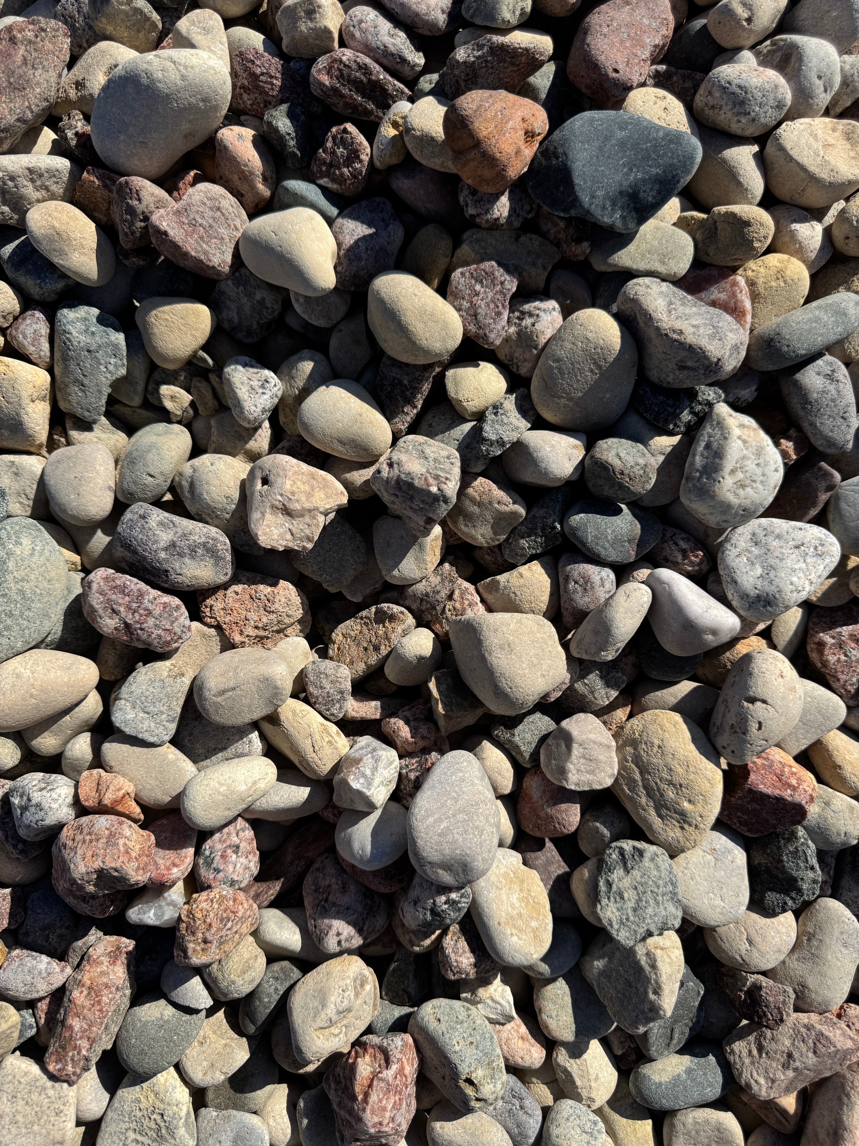 Close-up pile of smooth Patriot Rock river pebbles in tans, grays, and reds